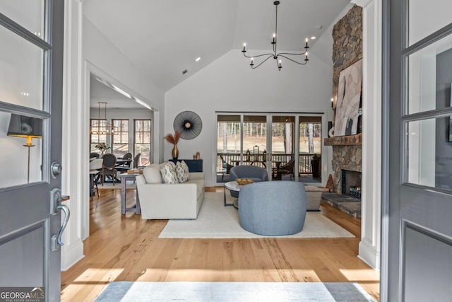 living room with a stone fireplace, high vaulted ceiling, light hardwood / wood-style flooring, and a notable chandelier