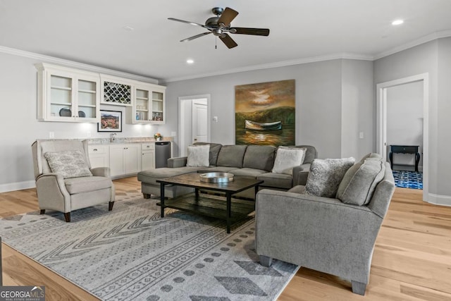 living room featuring crown molding, wet bar, ceiling fan, and light wood-type flooring