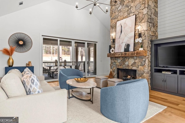 living room with wood-type flooring, a stone fireplace, a chandelier, and high vaulted ceiling