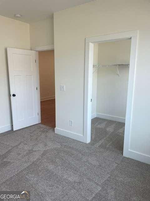 unfurnished bedroom featuring dark carpet, a walk in closet, and a closet