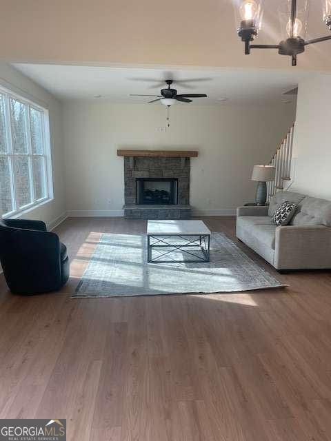 living room with hardwood / wood-style floors, a stone fireplace, and ceiling fan with notable chandelier