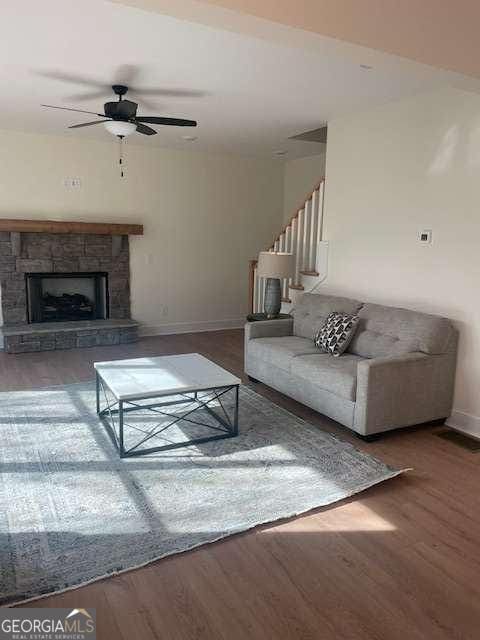 unfurnished living room with wood-type flooring, a stone fireplace, and ceiling fan