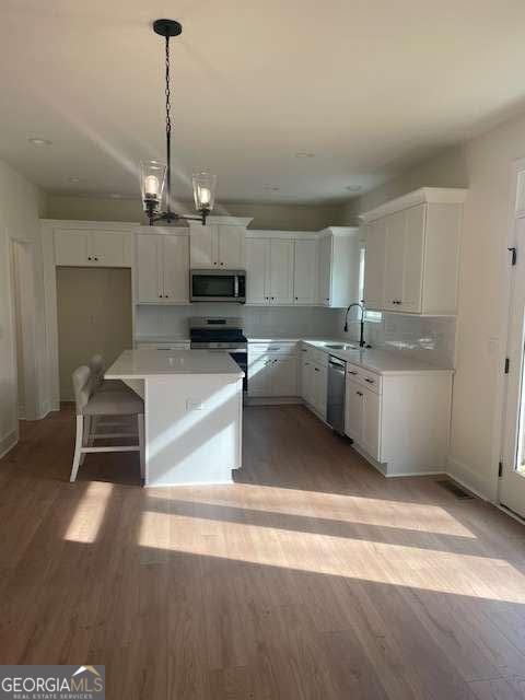 kitchen featuring hardwood / wood-style floors, stainless steel appliances, white cabinets, a kitchen island, and decorative light fixtures