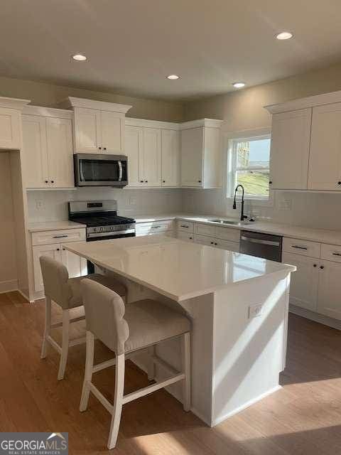 kitchen with a kitchen island, white cabinetry, wood-type flooring, sink, and stainless steel appliances