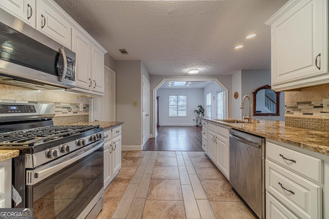 kitchen with white cabinetry, stainless steel appliances, sink, and light stone counters