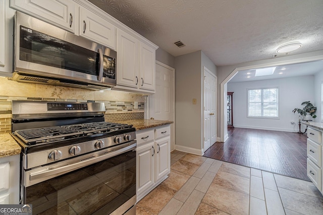 kitchen with appliances with stainless steel finishes, white cabinets, decorative backsplash, light stone countertops, and a textured ceiling