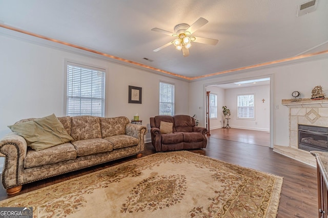 living room with a tiled fireplace, ornamental molding, ceiling fan, and dark hardwood / wood-style flooring