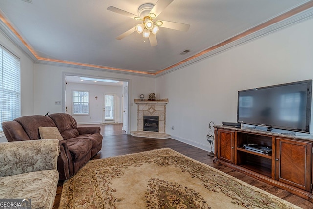 living room featuring a tile fireplace, ornamental molding, dark wood-type flooring, and ceiling fan