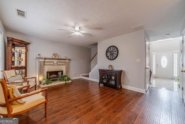 living room with a tiled fireplace, ceiling fan, dark wood-type flooring, and a textured ceiling