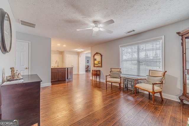 living area featuring sink, a textured ceiling, dark wood-type flooring, and ceiling fan