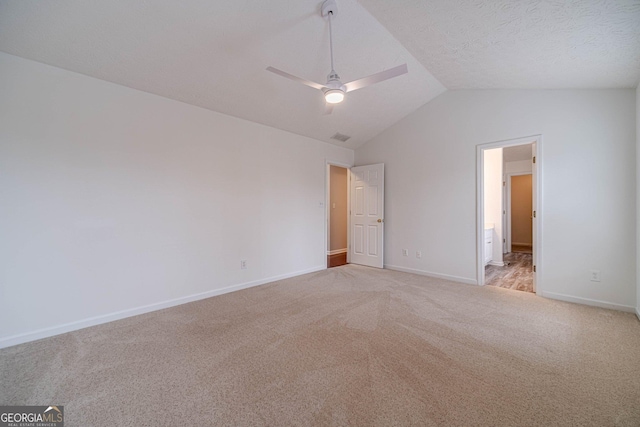 unfurnished bedroom with ensuite bath, ceiling fan, a textured ceiling, vaulted ceiling, and light colored carpet