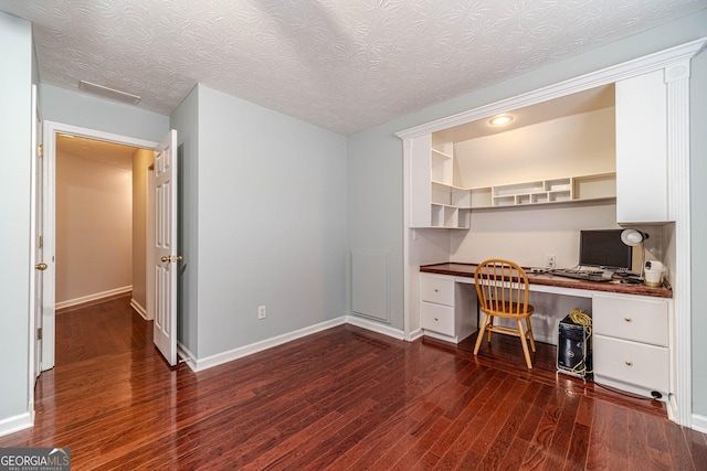 home office featuring dark hardwood / wood-style floors, built in desk, and a textured ceiling