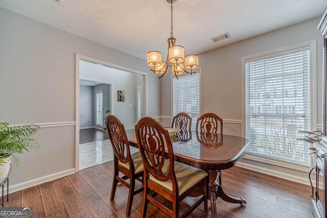 dining room featuring dark wood-type flooring, a wealth of natural light, a notable chandelier, and a textured ceiling