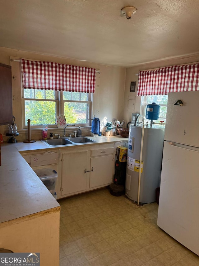 kitchen with white refrigerator, white cabinetry, sink, and electric water heater