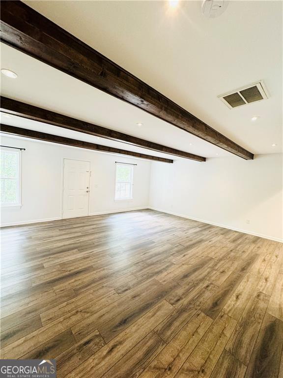 unfurnished living room featuring wood-type flooring and beam ceiling