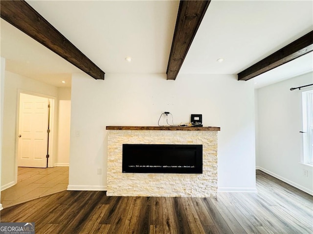 unfurnished living room with hardwood / wood-style flooring, a stone fireplace, and beamed ceiling