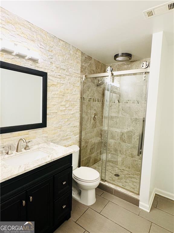 bathroom featuring a shower with door, vanity, tile patterned floors, and toilet