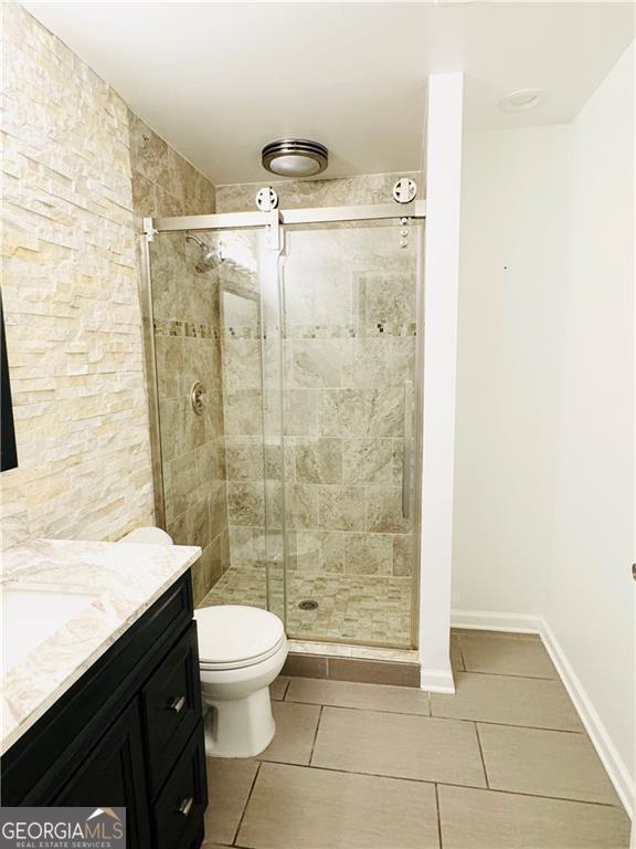 bathroom with a shower with door, vanity, tile patterned floors, and toilet