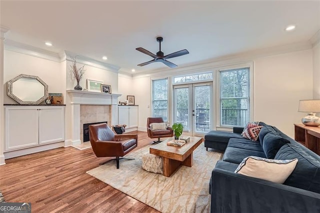 living room featuring crown molding, ceiling fan, a fireplace, french doors, and light wood-type flooring