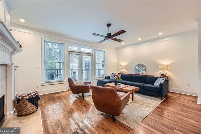 living room featuring french doors, crown molding, light hardwood / wood-style flooring, ceiling fan, and a tiled fireplace