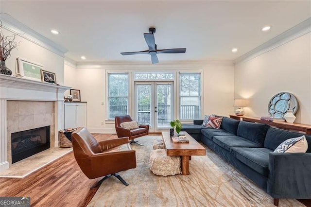 living room with crown molding, a tile fireplace, french doors, and light wood-type flooring