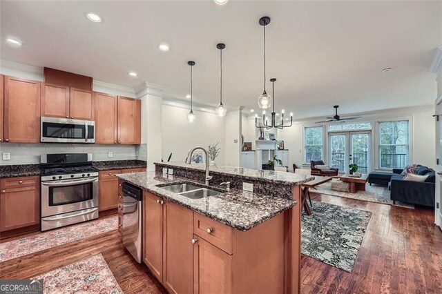 kitchen with sink, hanging light fixtures, dark stone countertops, a center island with sink, and appliances with stainless steel finishes