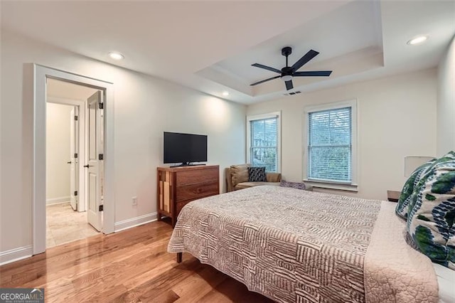 bedroom featuring light hardwood / wood-style flooring, ceiling fan, and a tray ceiling