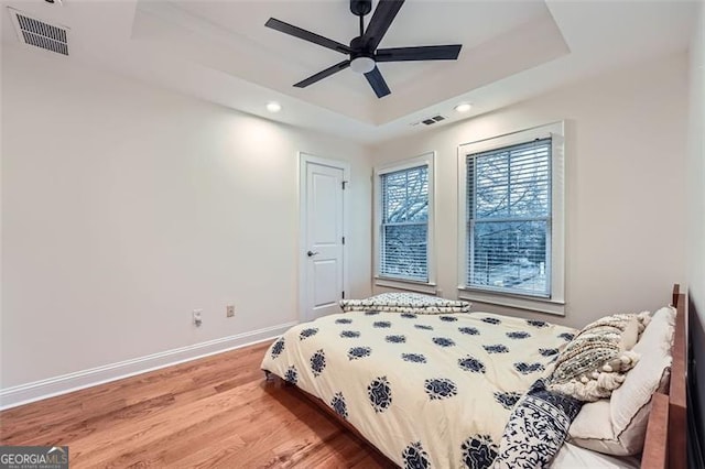 bedroom with wood-type flooring, ceiling fan, and a tray ceiling