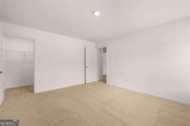 unfurnished bedroom with a walk in closet and light colored carpet