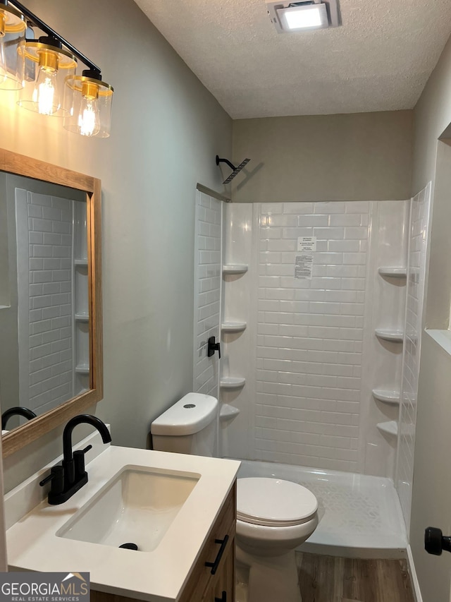 bathroom featuring wood-type flooring, vanity, walk in shower, toilet, and a textured ceiling