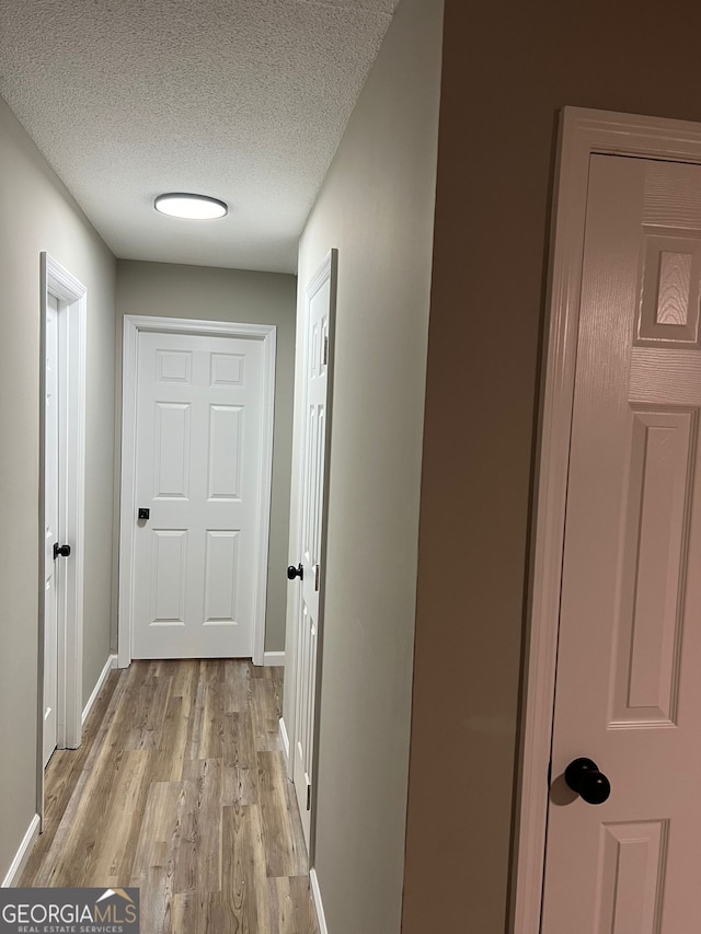 corridor with a textured ceiling and light wood-type flooring