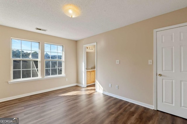 unfurnished bedroom featuring hardwood / wood-style floors, ensuite bath, and a textured ceiling