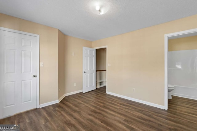 unfurnished bedroom featuring ensuite bathroom, dark hardwood / wood-style floors, and a textured ceiling