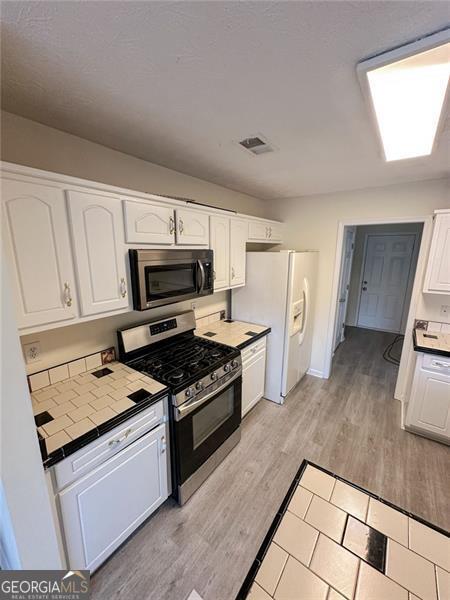 kitchen featuring light hardwood / wood-style flooring, tile counters, stainless steel appliances, and white cabinets