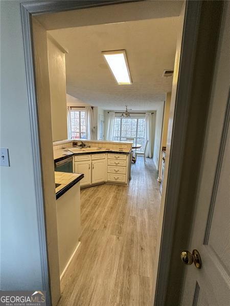 kitchen featuring white cabinetry, stainless steel dishwasher, kitchen peninsula, and light hardwood / wood-style floors