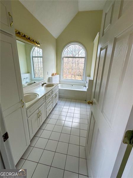 bathroom with lofted ceiling, a healthy amount of sunlight, tile patterned flooring, and a tub