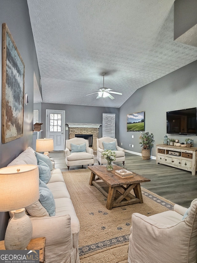 living room with vaulted ceiling, a fireplace, wood-type flooring, ceiling fan, and a textured ceiling