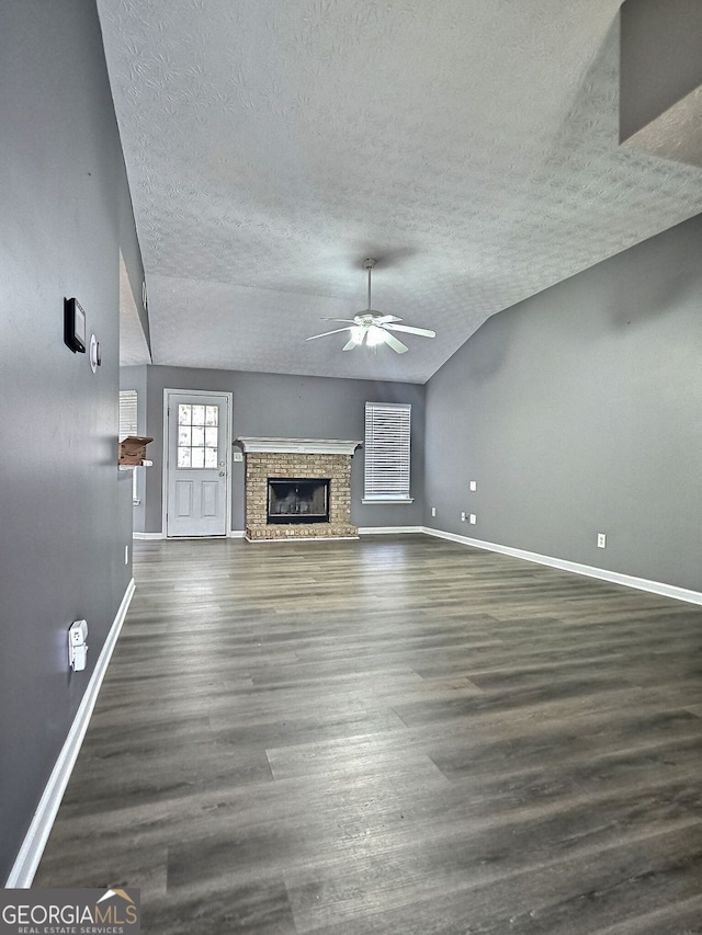 unfurnished living room with dark wood-type flooring, lofted ceiling, a brick fireplace, a textured ceiling, and ceiling fan