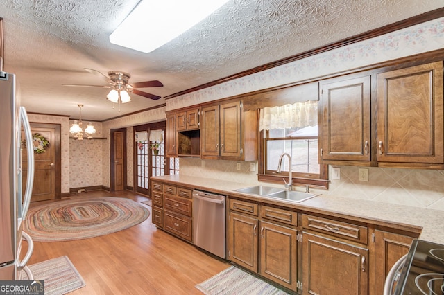 kitchen with pendant lighting, sink, ornamental molding, stainless steel appliances, and light hardwood / wood-style flooring