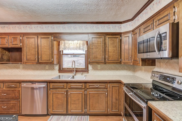 kitchen with appliances with stainless steel finishes, sink, a textured ceiling, and light wood-type flooring