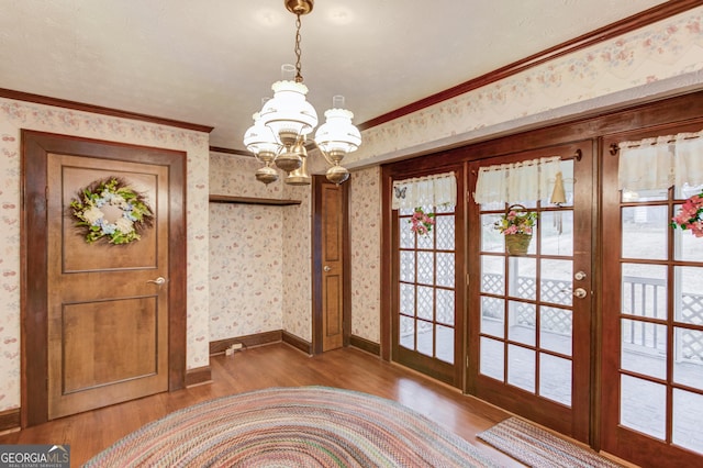 doorway with french doors, wood-type flooring, crown molding, and a chandelier