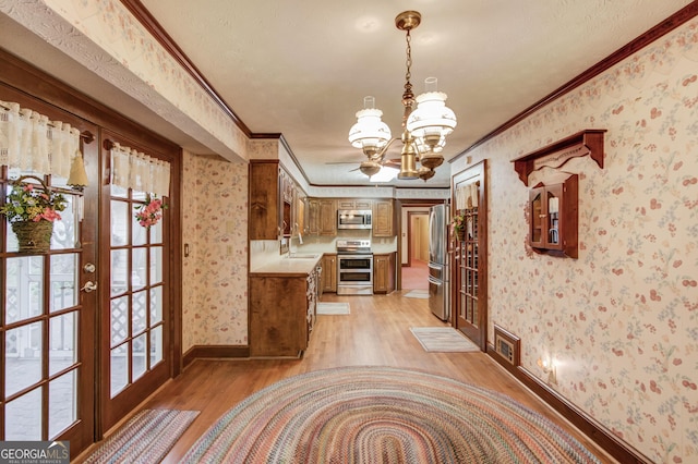 interior space featuring a chandelier, ornamental molding, stainless steel appliances, light wood-type flooring, and french doors