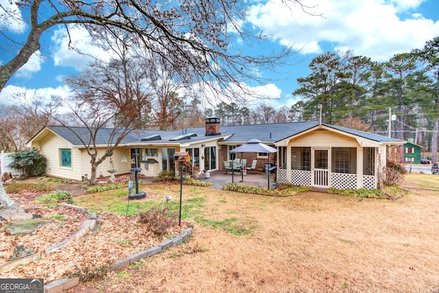 rear view of house featuring a sunroom, a patio, and a lawn