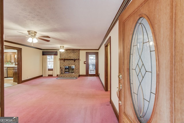 unfurnished living room with crown molding, ceiling fan, a fireplace, carpet floors, and a textured ceiling