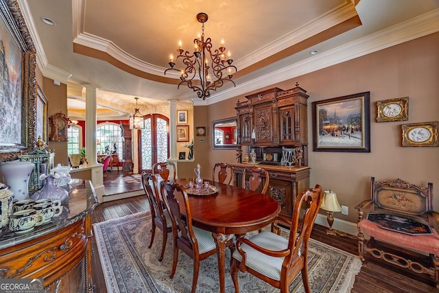 dining space featuring decorative columns, ornamental molding, a notable chandelier, a raised ceiling, and dark wood-type flooring