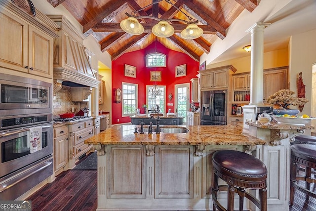 kitchen featuring sink, stainless steel appliances, decorative columns, an island with sink, and wooden ceiling