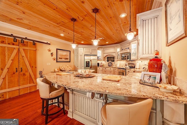 kitchen with appliances with stainless steel finishes, a barn door, kitchen peninsula, and hanging light fixtures