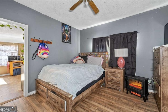 bedroom with lofted ceiling, wood-type flooring, a textured ceiling, and a wood stove