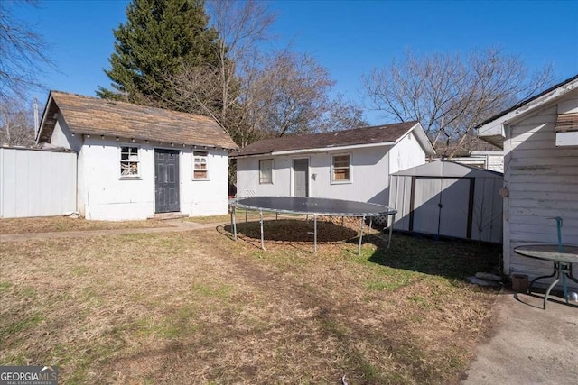 back of house featuring a lawn, a trampoline, and a storage unit