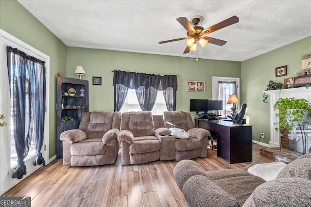 living room featuring ceiling fan, a fireplace, light hardwood / wood-style floors, and a textured ceiling